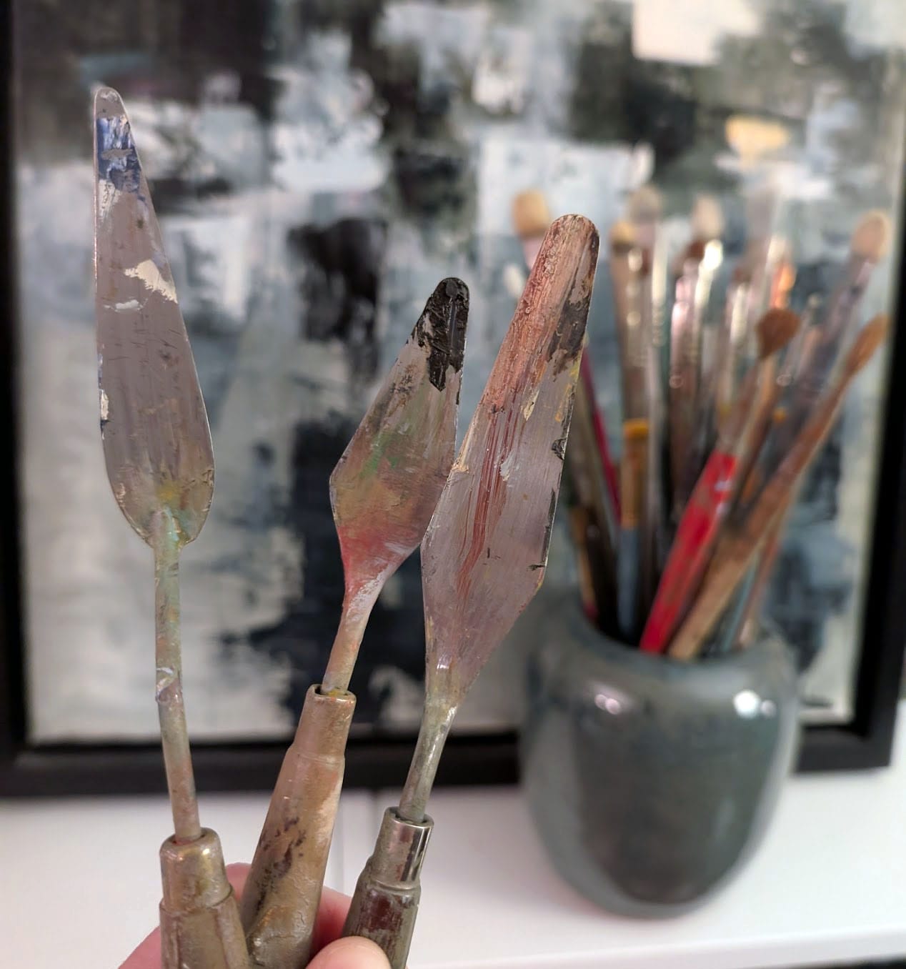 Three metal palette knives covered in colorful dabs of dried paint.