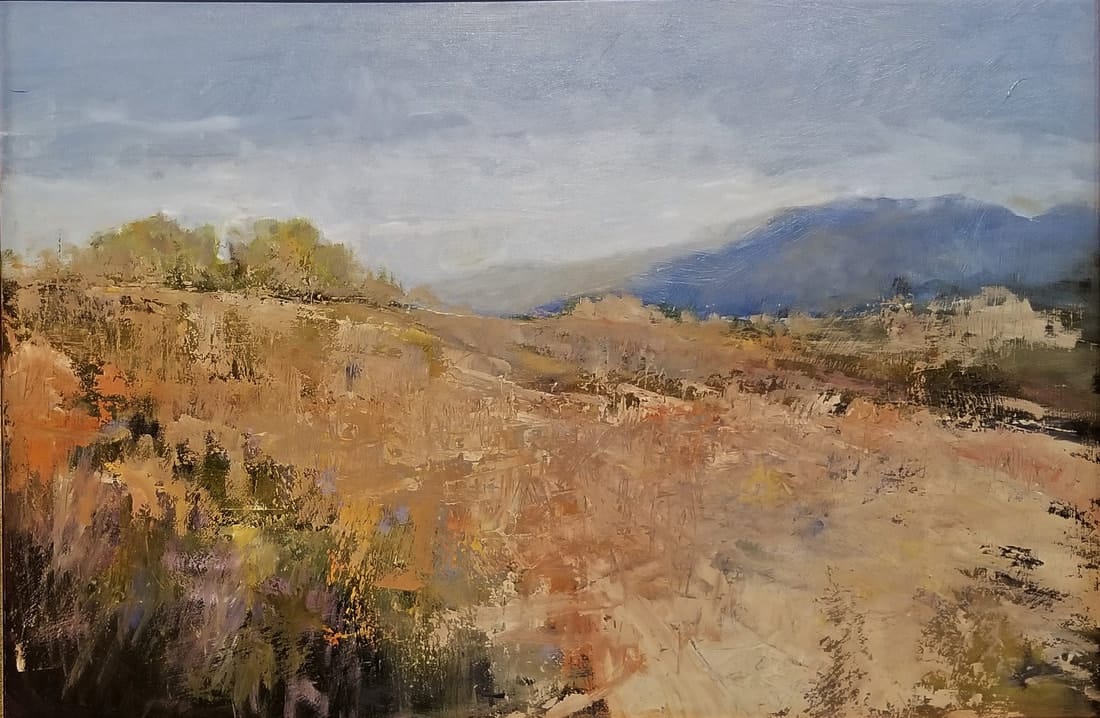 An abstract desert landscape in taupes and yellows, blue mountains looming in the distance.