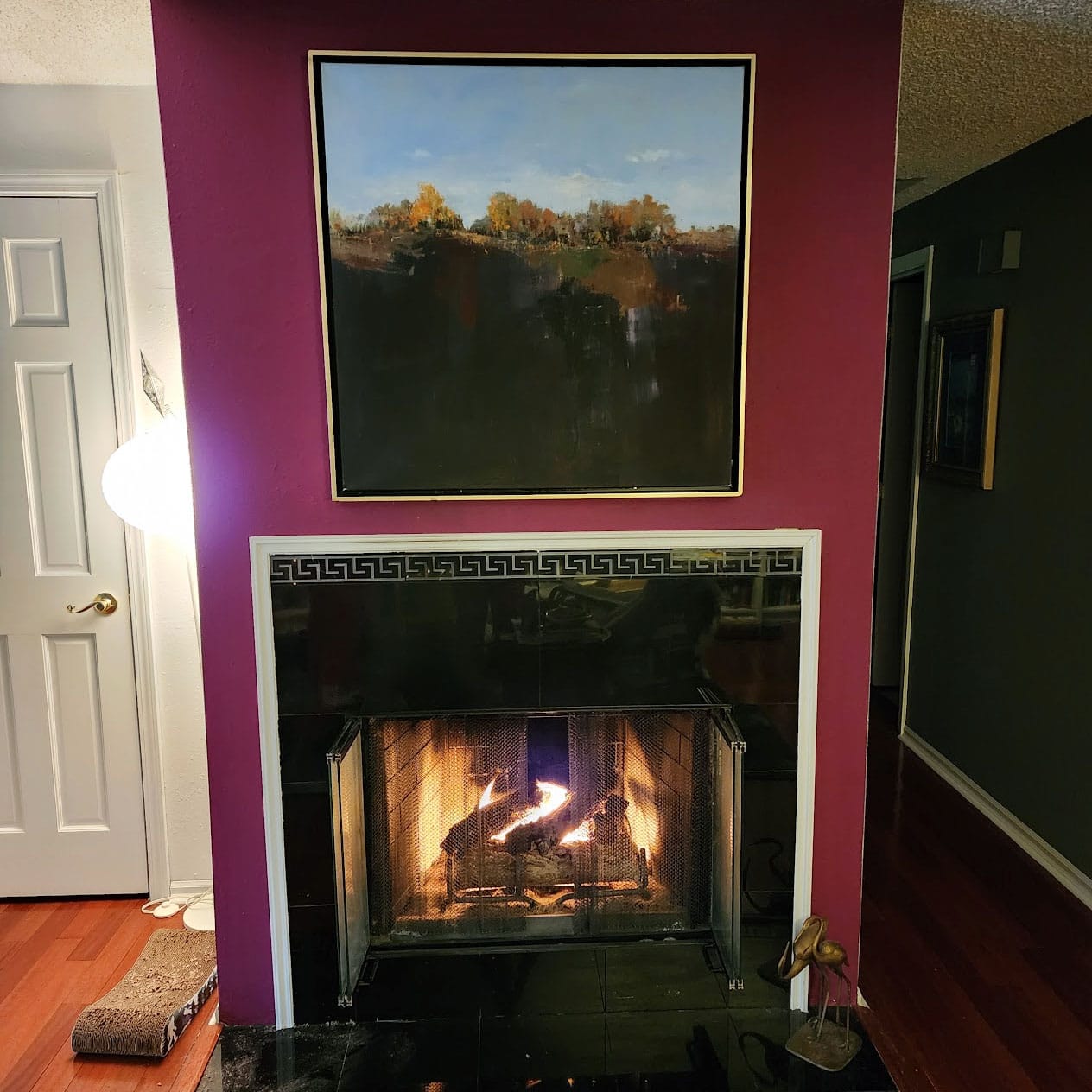 Over a lit fireplace hands a large square landscape painting. 2/3rds of the canvas is underground, dark and layered. After the surface, autumn trees and blue sky.